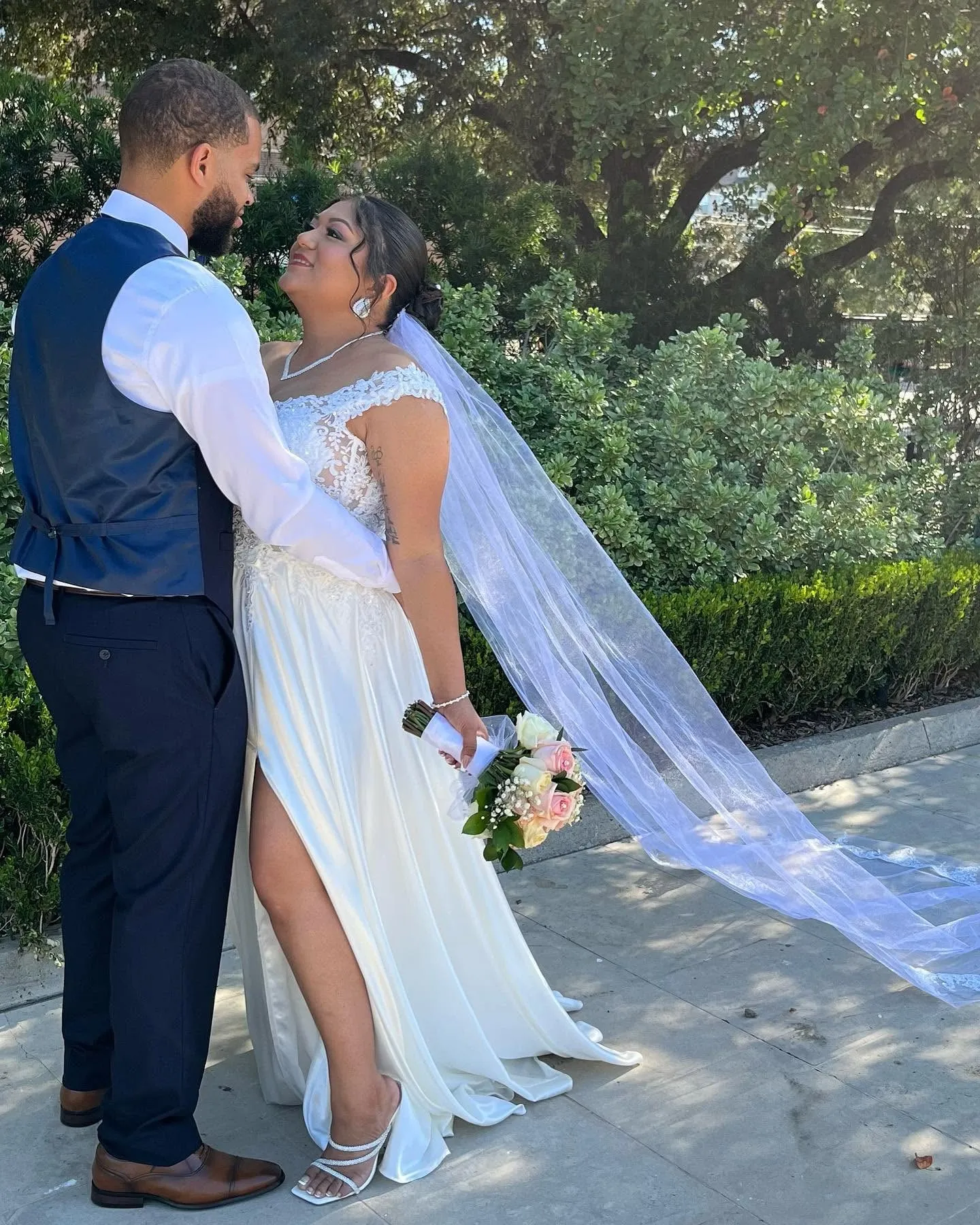 Newlywed couple sharing a quiet moment outdoors with the bride’s long veil flowing behind her
