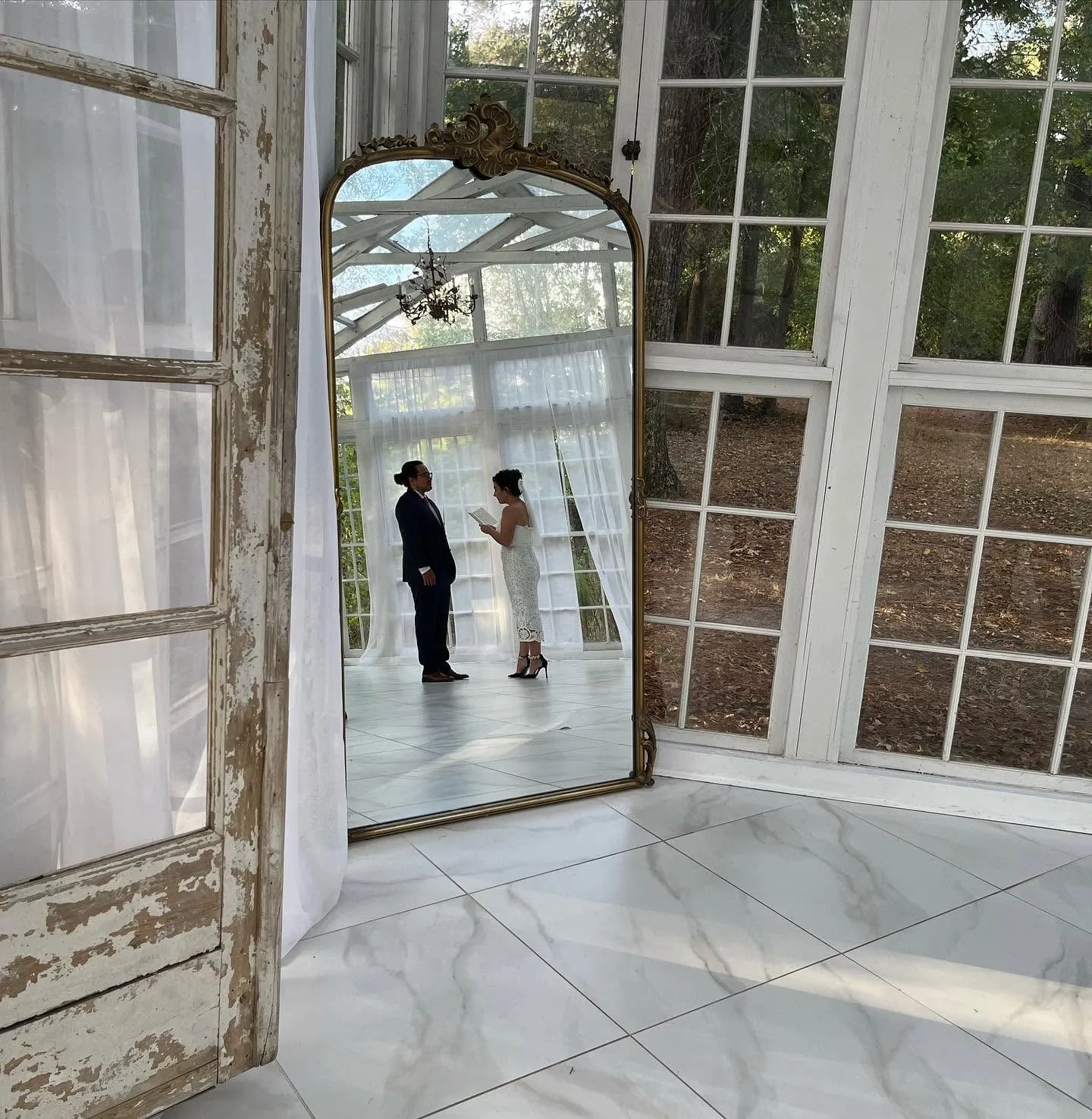 Newlywed couple reflected in a tall antique mirror inside a bright venue